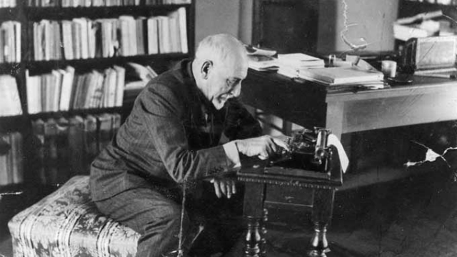 Foto in bianco e nero di un anziano Luigi Pirandello, chino sulla macchina da scrivere nel suo studio.
